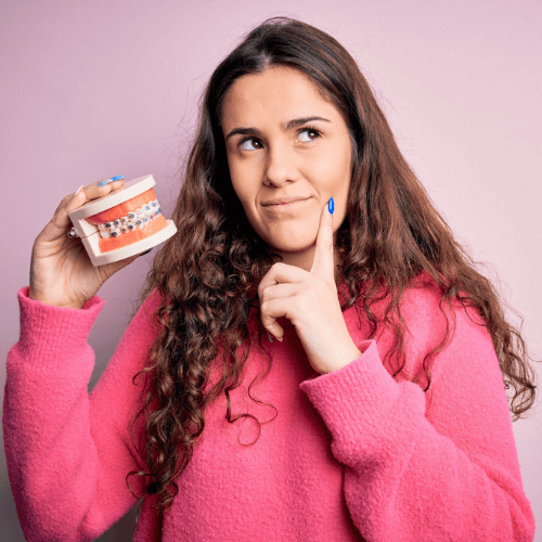 A woman deciding what braces to get, holding a model of some teeth with braces on, in Manchester