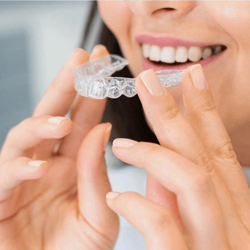 woman holding clear new Invisalign aligners whilst smiling.