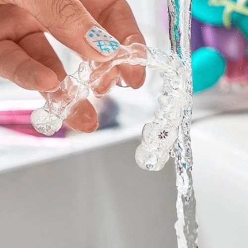 clear invisalign braces being held under running water to be cleaned