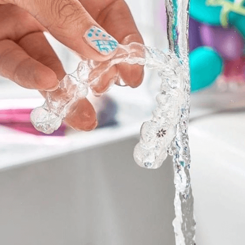 invisalign clear braces being held under running water to be cleaned