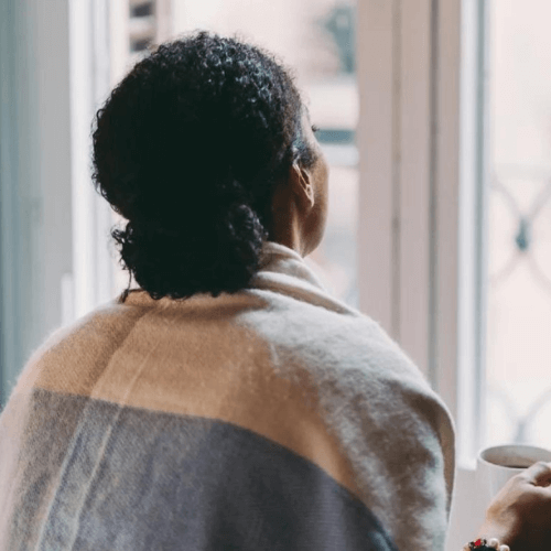 woman staying at home by the window, looking outside.