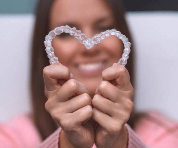 woman holding a heart shape made with invisalign clear braces