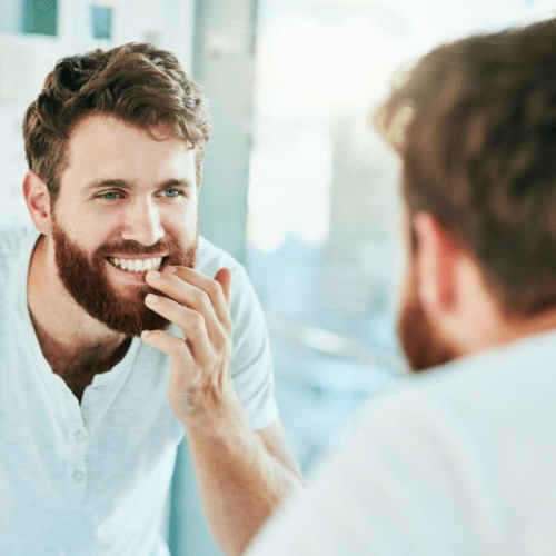 man checking his teeth in the mirror after brushing, in stockport, orthodontics