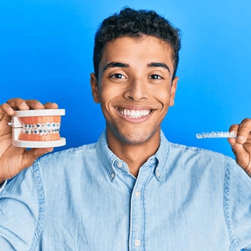 man holding dental model with metal braces and invisalign clear braces in other hand deciding between the options (Manchester)