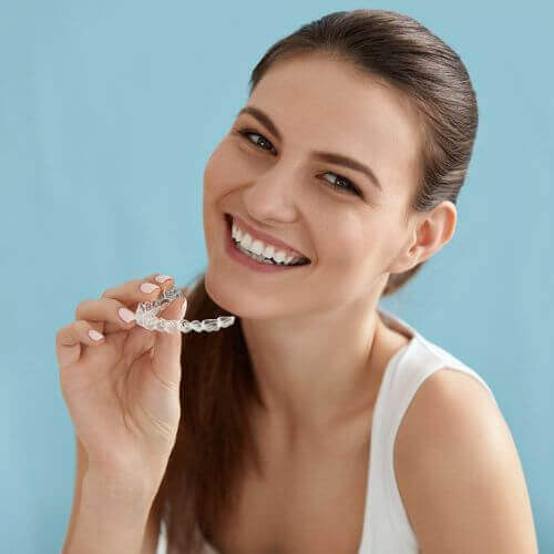 woman smiling at the camera with invisalign clear aligners in her hand stockport