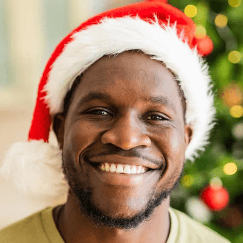 man with snow white teeth in santa hat looking at camera near a christmas tree at home. Greater manchester