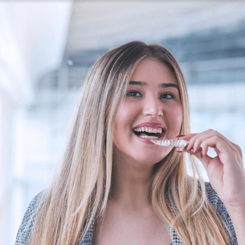 young woman putting her in clear braces whilst smiling